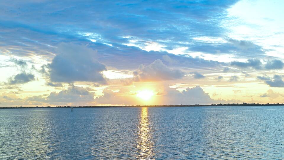 A sunset over a calm sea with a clear horizon and scattered clouds.