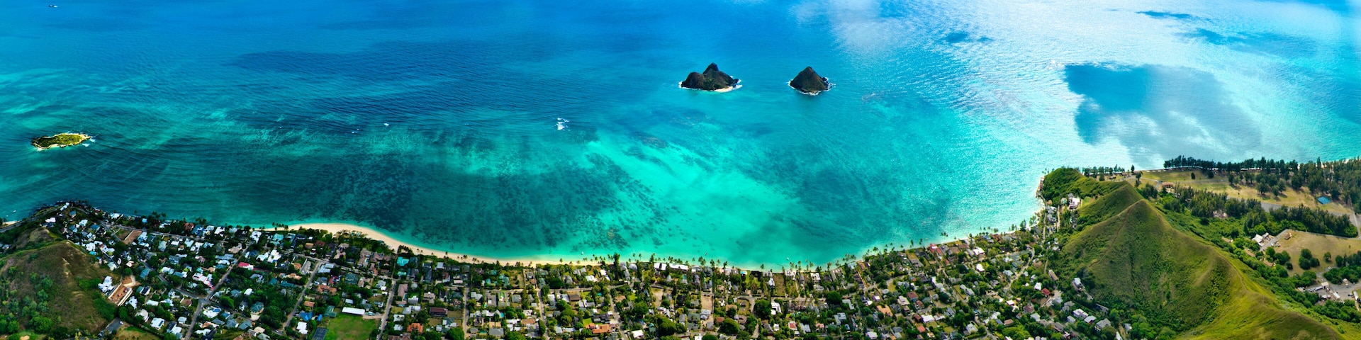 An aerial view of a coastal town with clear turquoise waters, two prominent islands, and lush green hills.