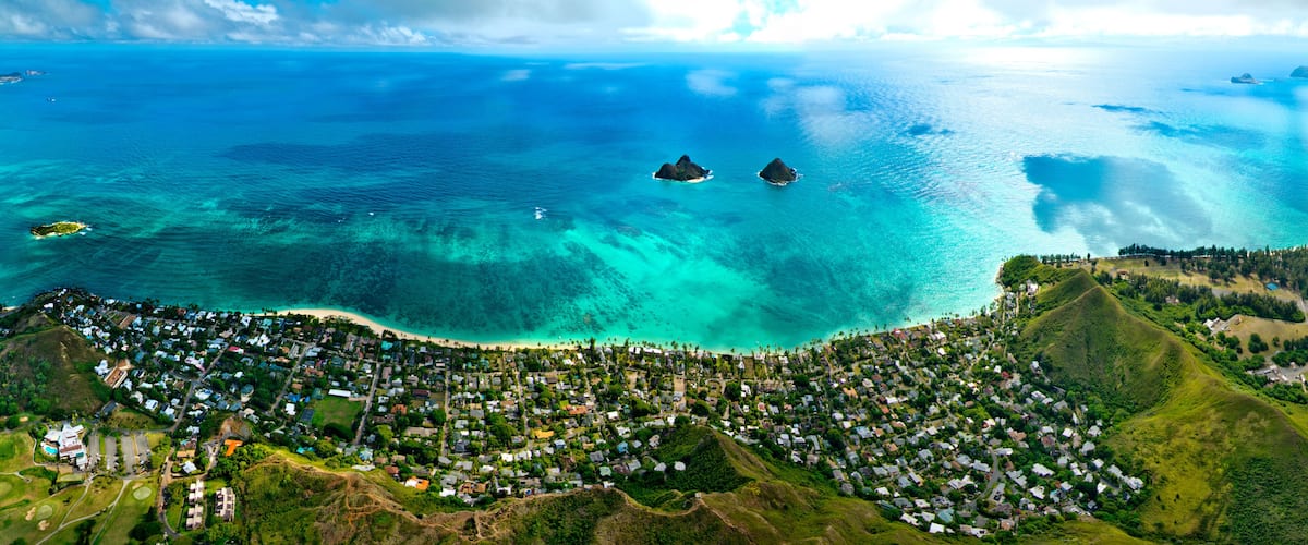 An aerial view of a coastal town with clear turquoise waters, two prominent islands, and lush green hills.
