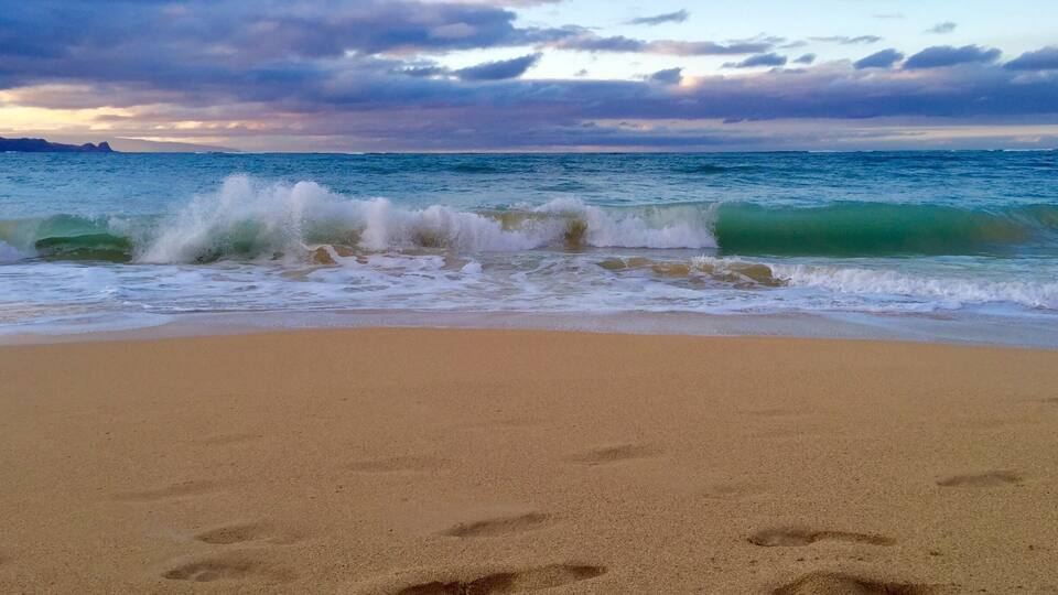 A beach with footprints in the sand and waves crashing onto the shore.