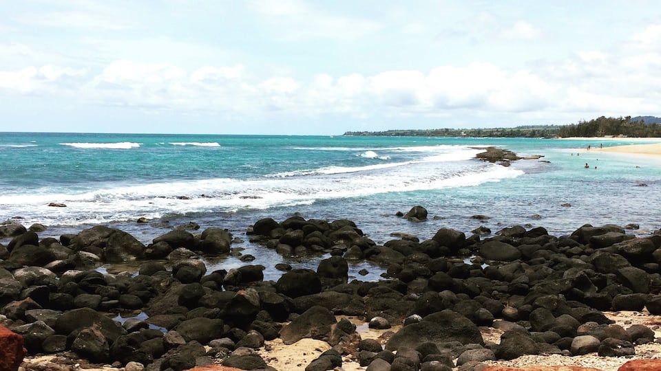 A rocky beach with waves crashing onto the shore and a clear blue sky.