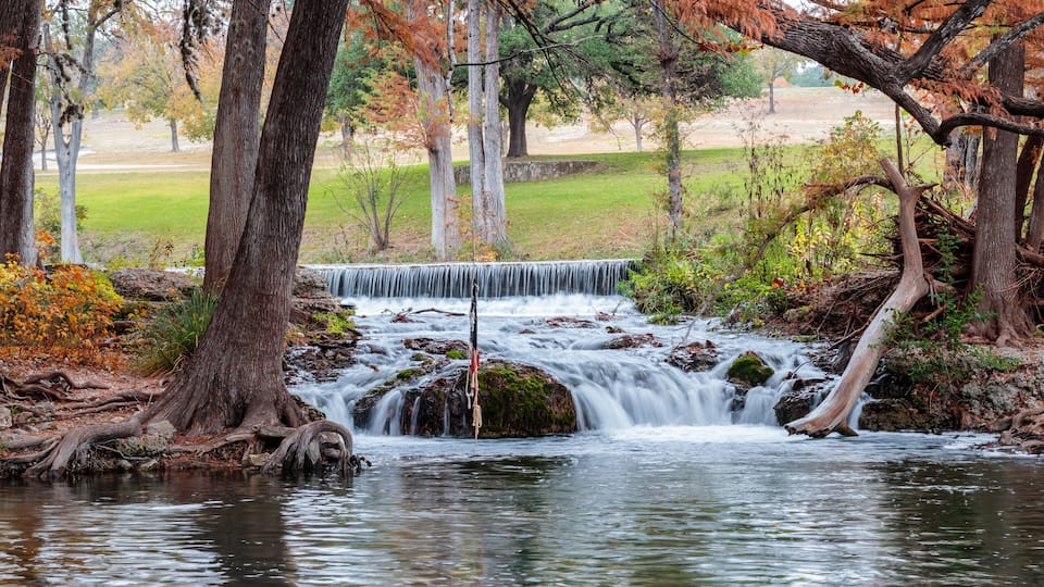 A waterfall in a forested area with autumn foliage.