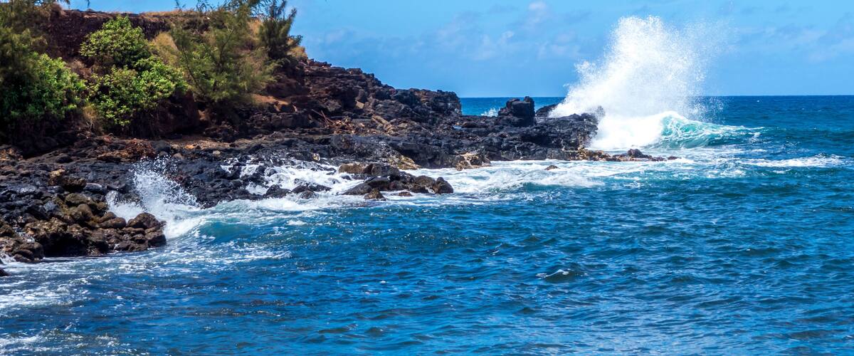 A rocky coastline with waves crashing against the rocks and a clear blue sky.