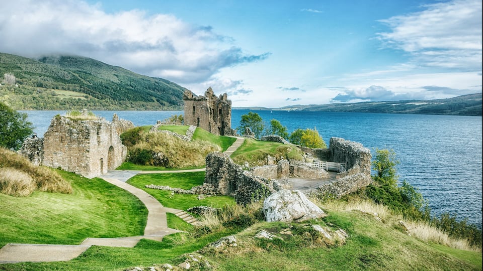 A historic castle ruin by a lake with a clear sky.