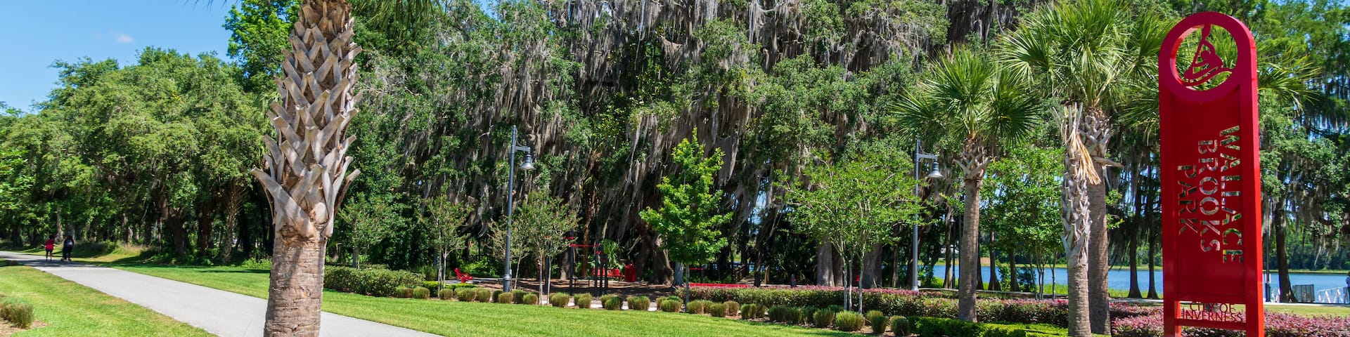 A park with a red sign, palm trees, and a crosswalk.