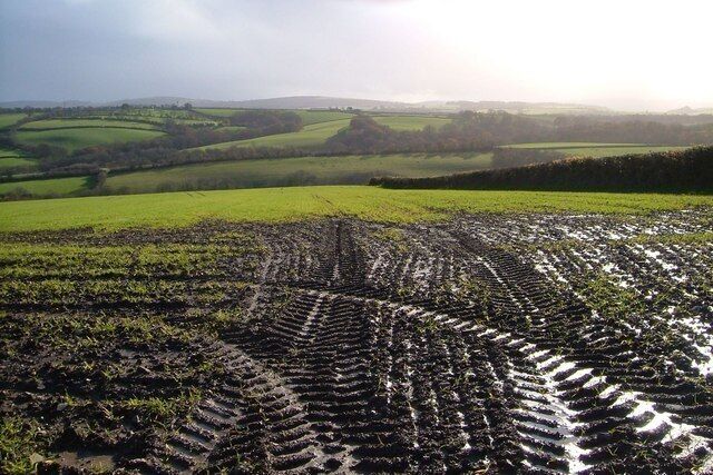 A rural landscape with a muddy field and rolling hills in the background.