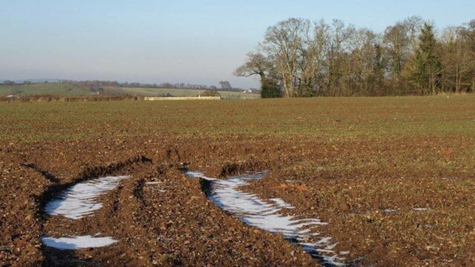 A muddy field with tire tracks and patches of snow.