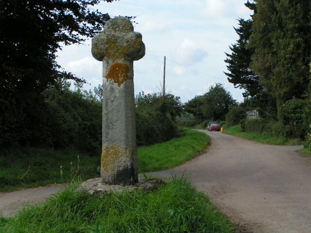A rural road with a stone cross and lush greenery.