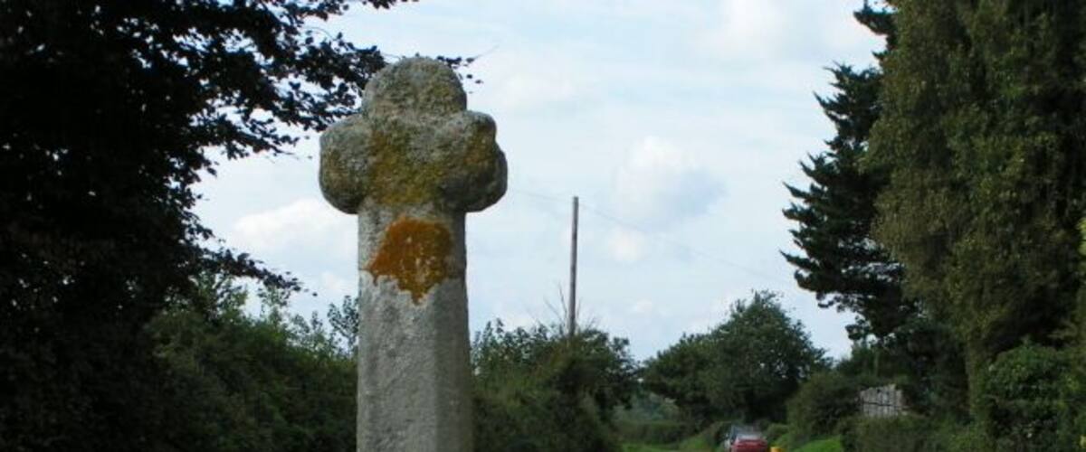 A rural road with a stone cross and lush greenery.