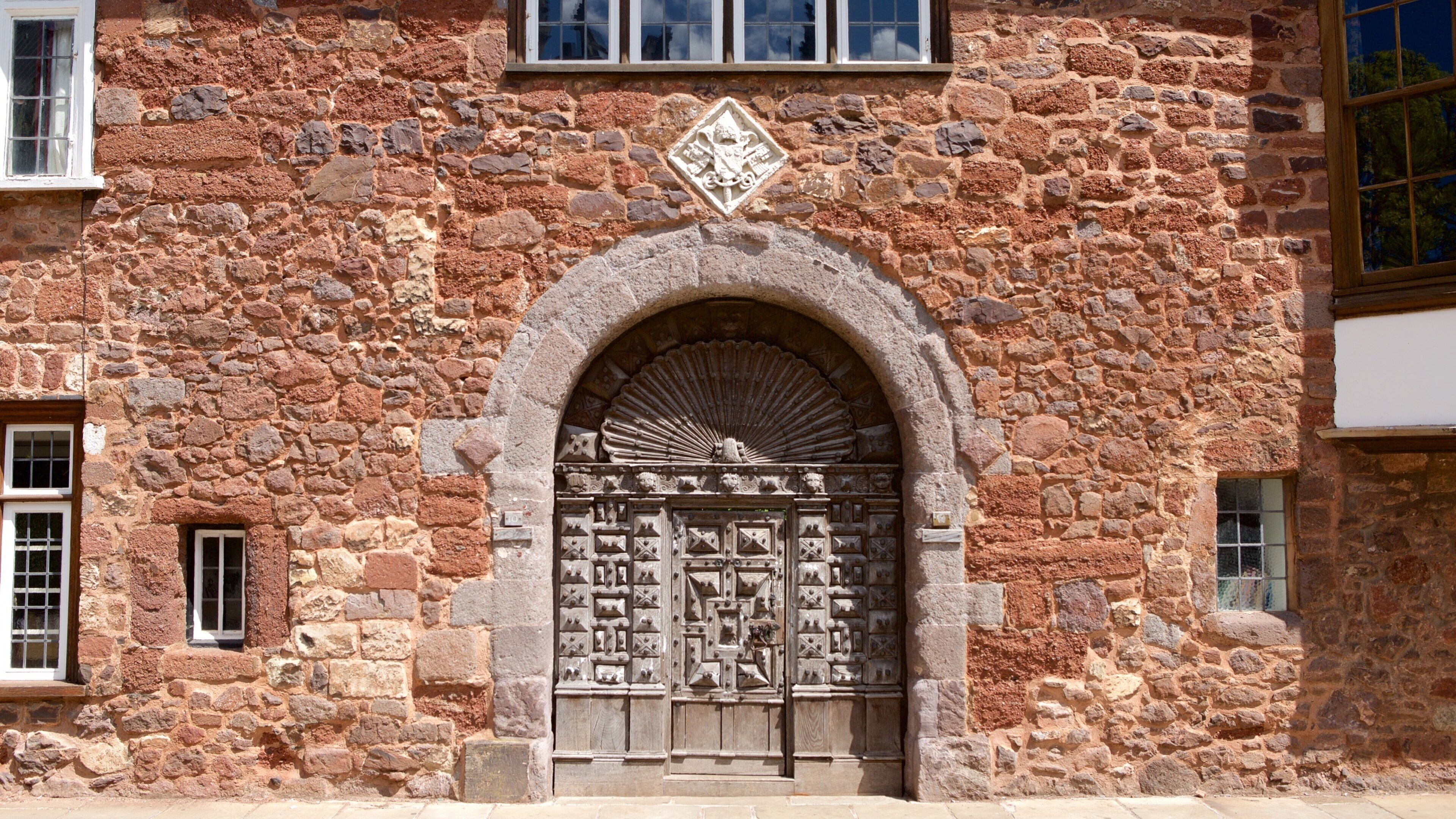 A stone building with a large arched entrance, intricate carvings, and a decorative emblem above the door.