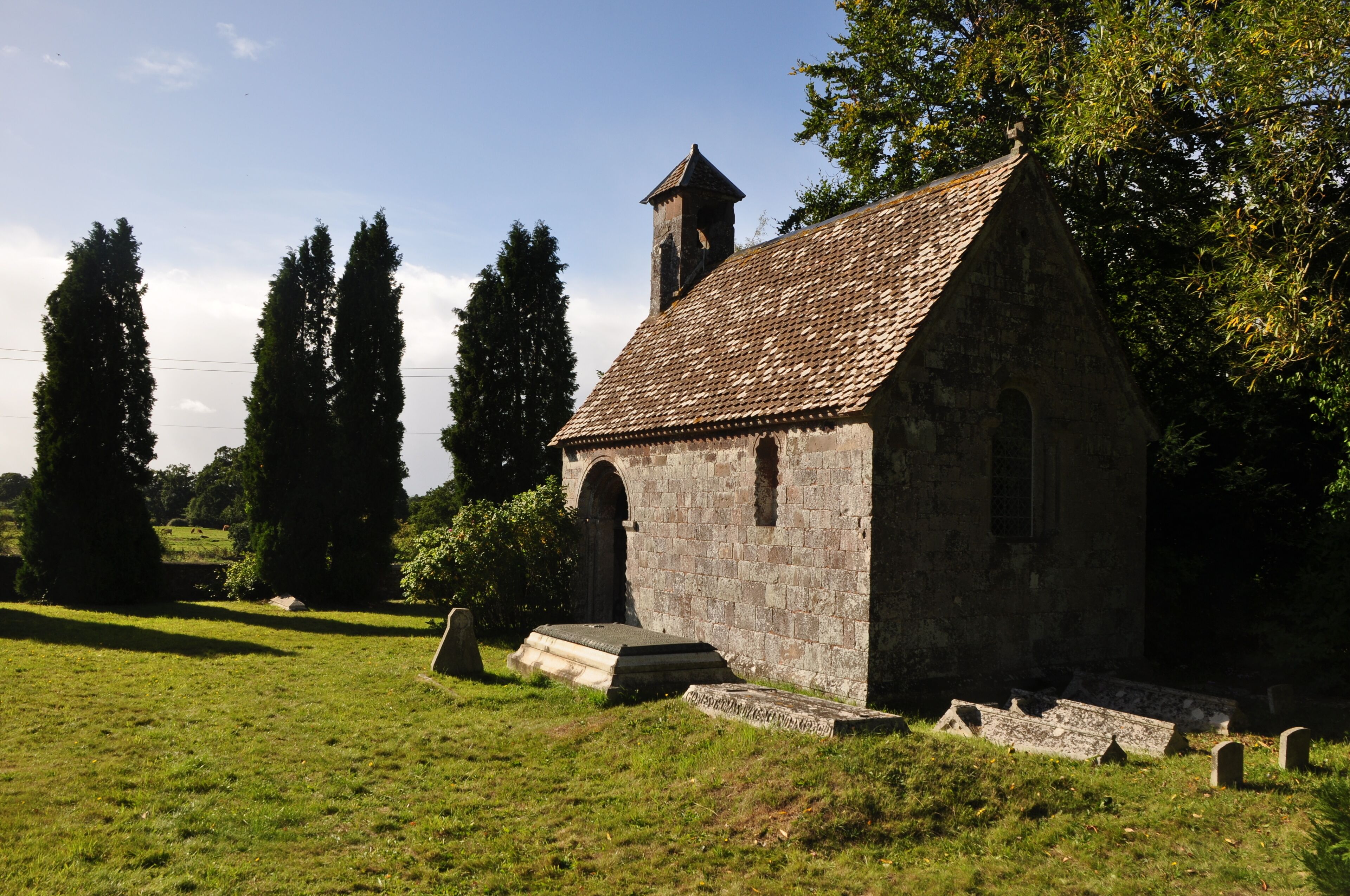 A small stone church with a tiled roof, surrounded by grass and trees.