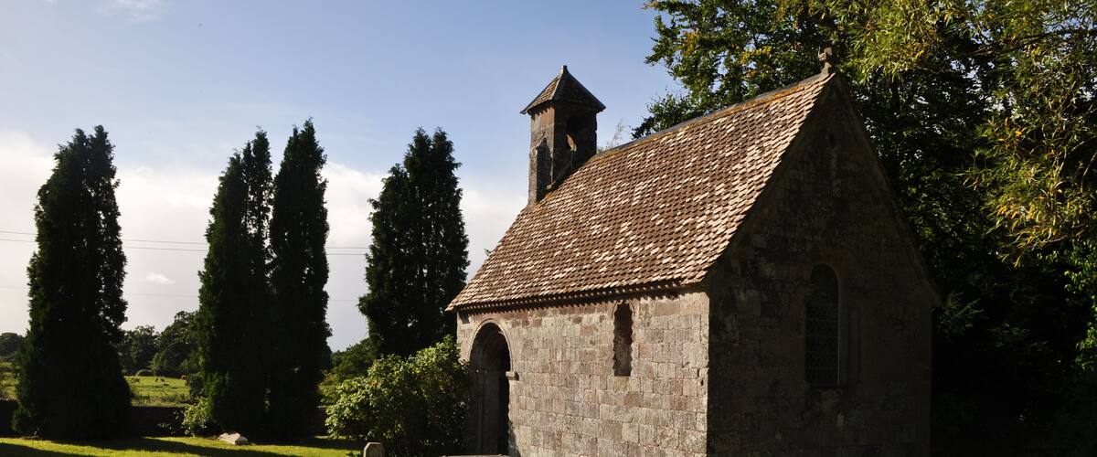 A small stone church with a tiled roof, surrounded by grass and trees.