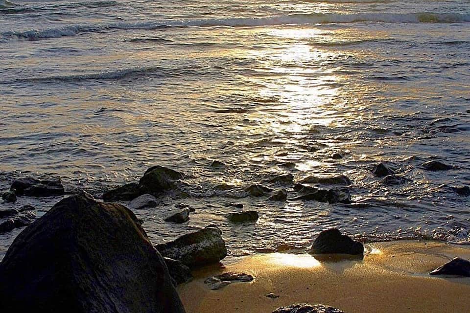 A beach with rocks and waves at sunset.