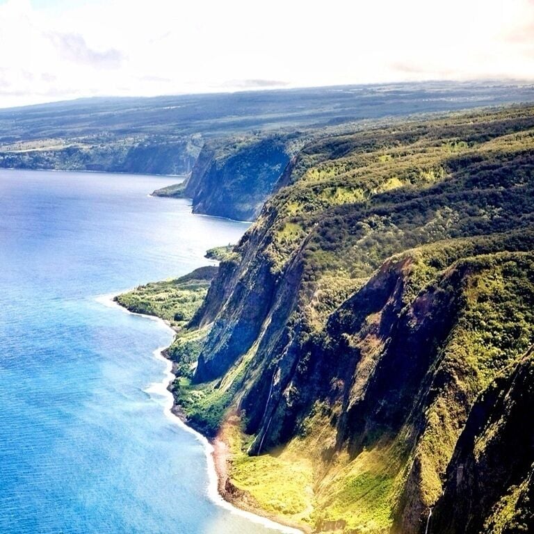 A coastal landscape with steep cliffs, a beach, and a clear blue ocean.