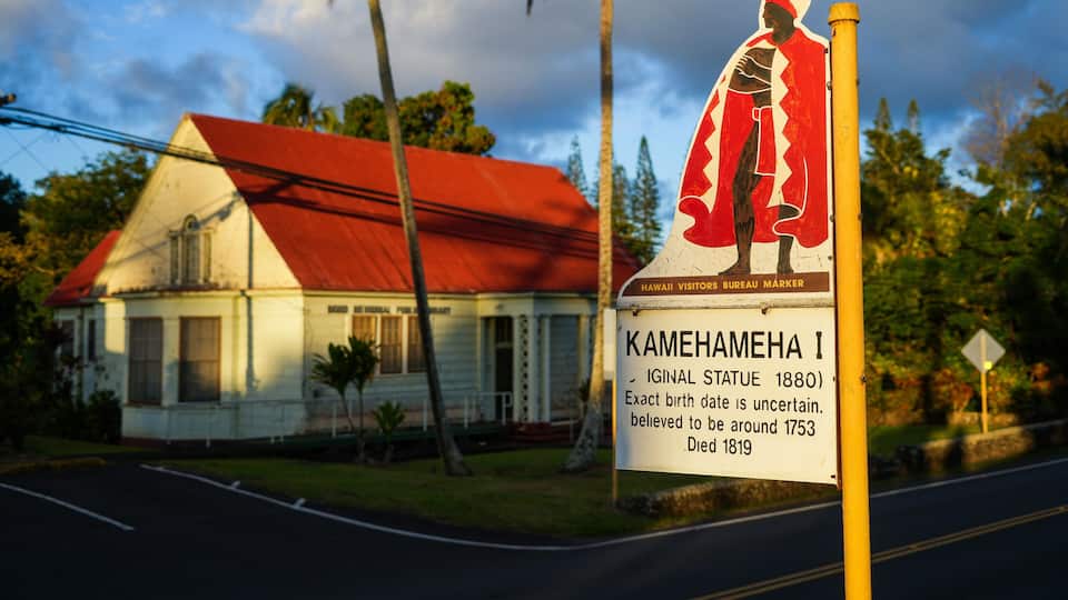 A historical marker for Kamehameha I, a statue, and a white house with a red roof.