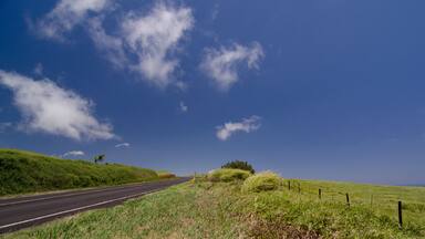 A rural road with grassy hills and a clear blue sky.