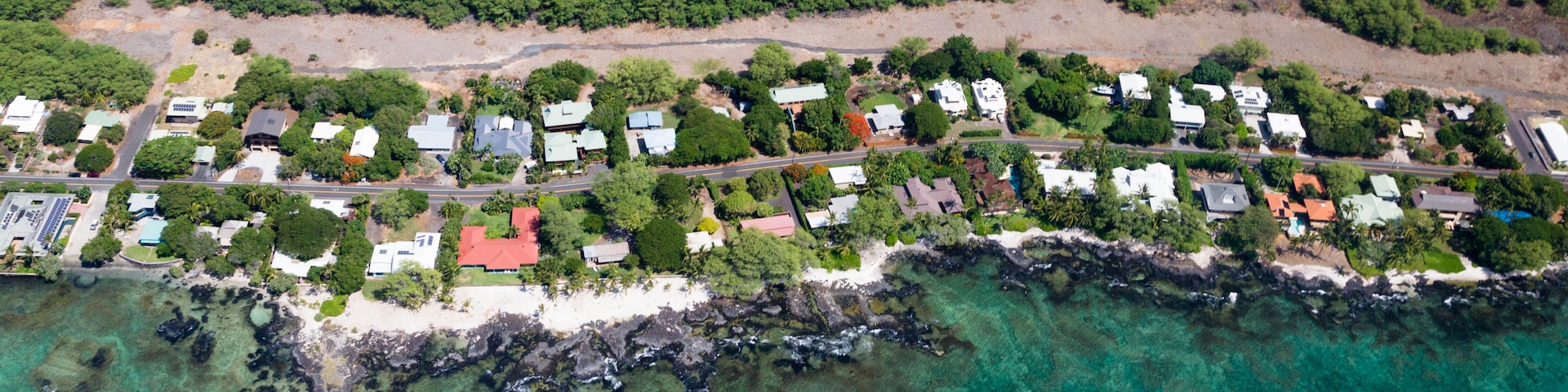 Vue aérienne d’une zone résidentielle côtière, avec des maisons, une plage et des eaux turquoise limpides.