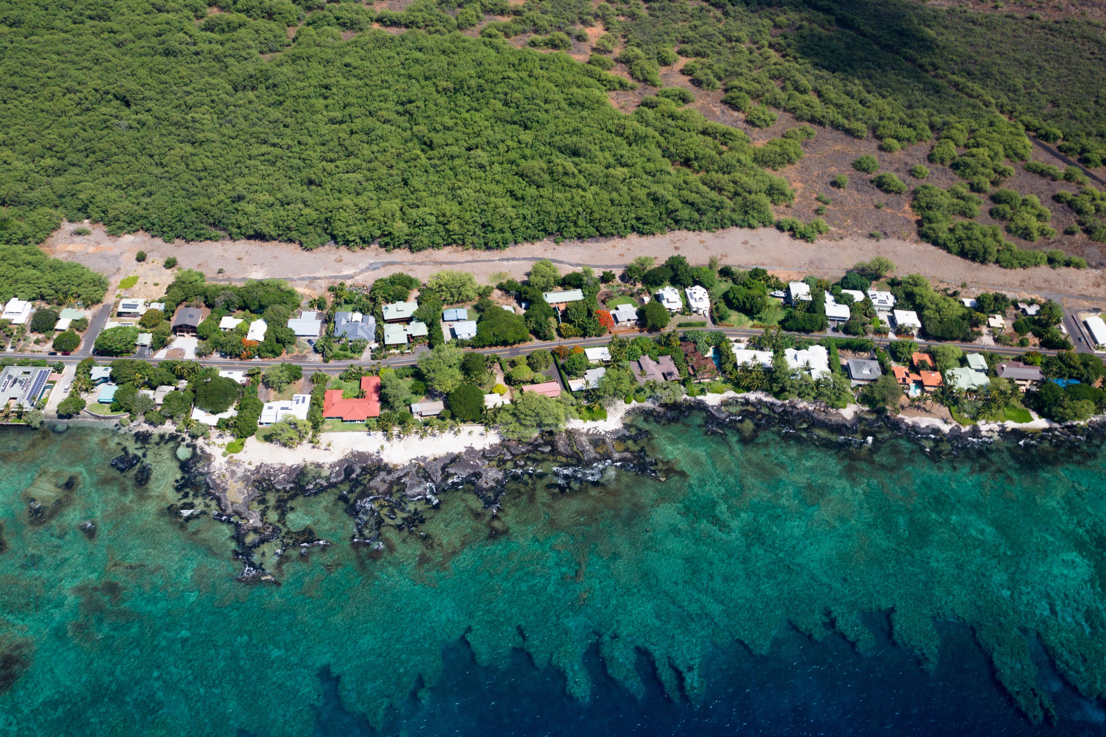 An aerial view of a coastal residential area with houses, a beach, and clear turquoise waters.