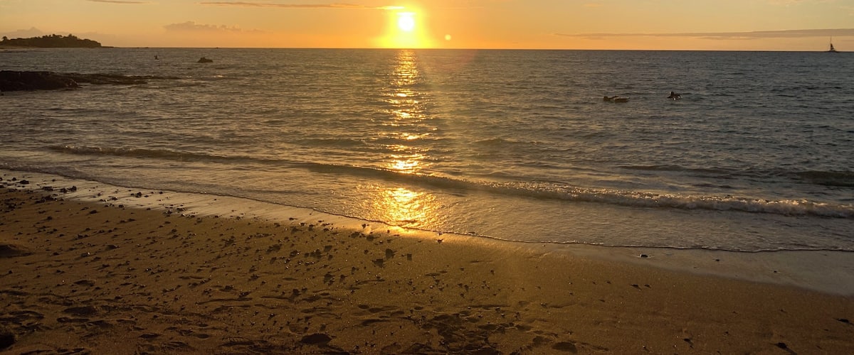 A sunset over a beach with waves and a distant sailboat.