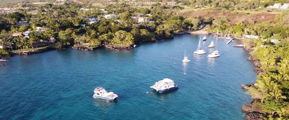 Aerial shot of Keauhou bay in Kailua Kona with boats on water surface and surrounded by vegetation