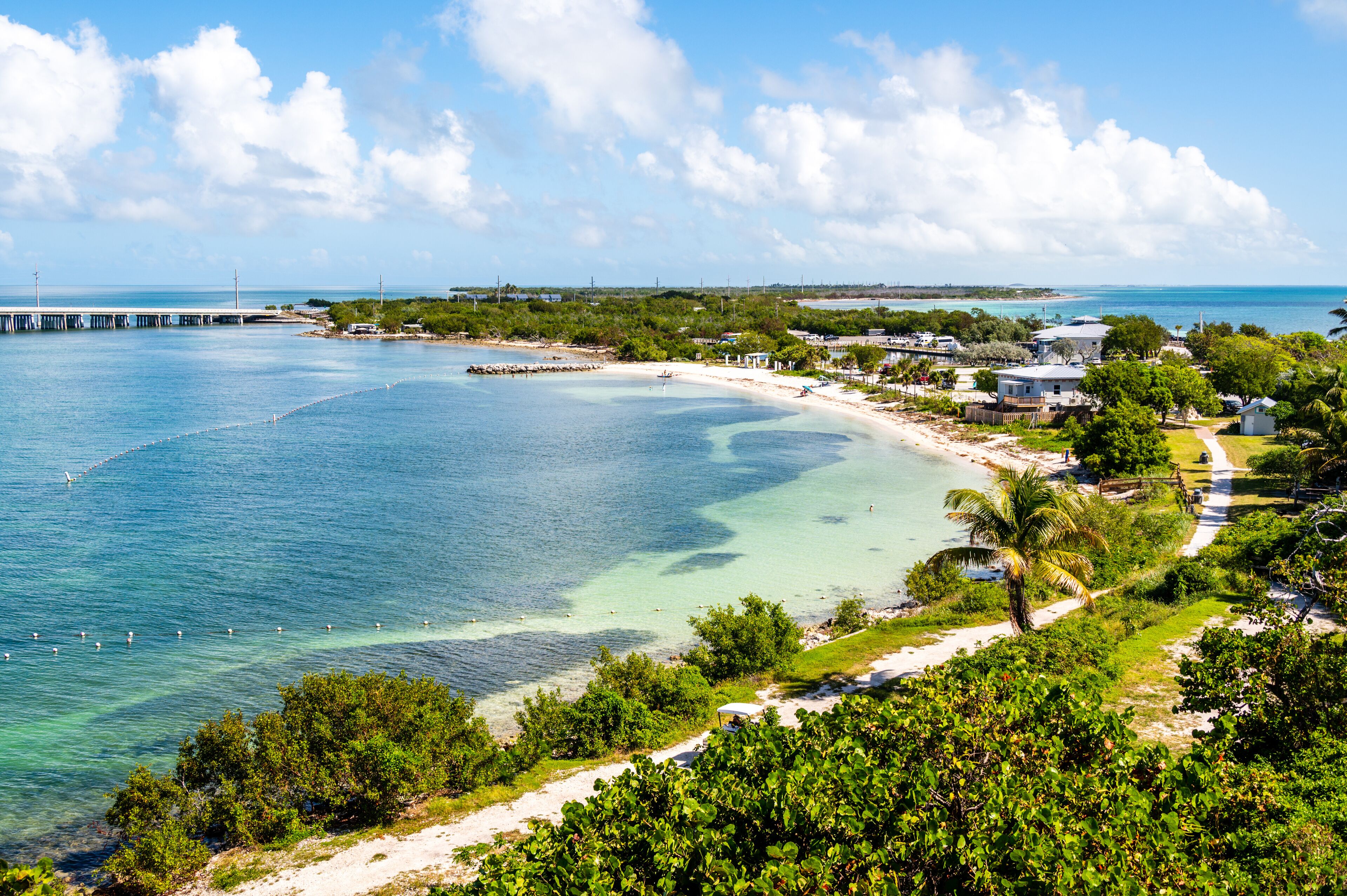 Uma vila costeira com praia, águas cristalinas, um cais e vegetação exuberante.