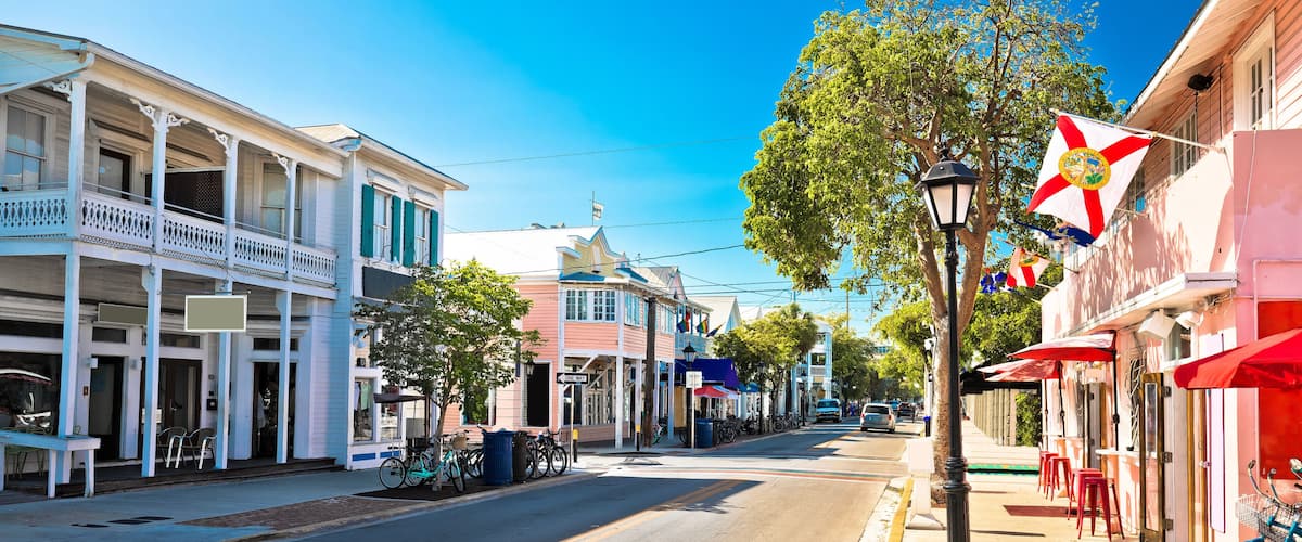 A sunny street lined with historic buildings, a 'ONE WAY' sign, and a flagpole with flags.