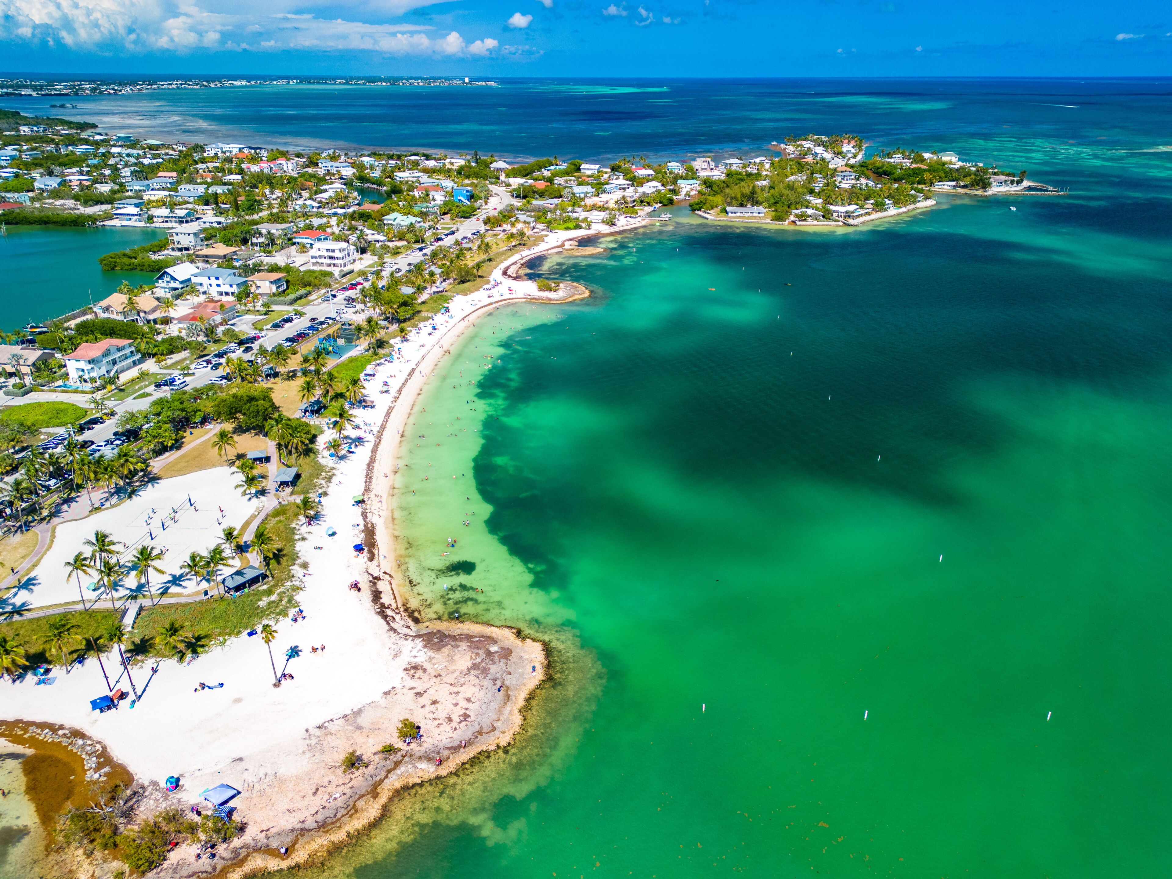 Un pueblo costero con playa, aguas turquesas cristalinas y una combinación de edificios residenciales y comerciales.