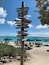 Een houten bord met plaatsnamen en afstanden, een strand met parasols en ligstoelen.