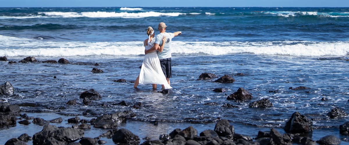 A couple standing on a rocky beach with the ocean in the background.