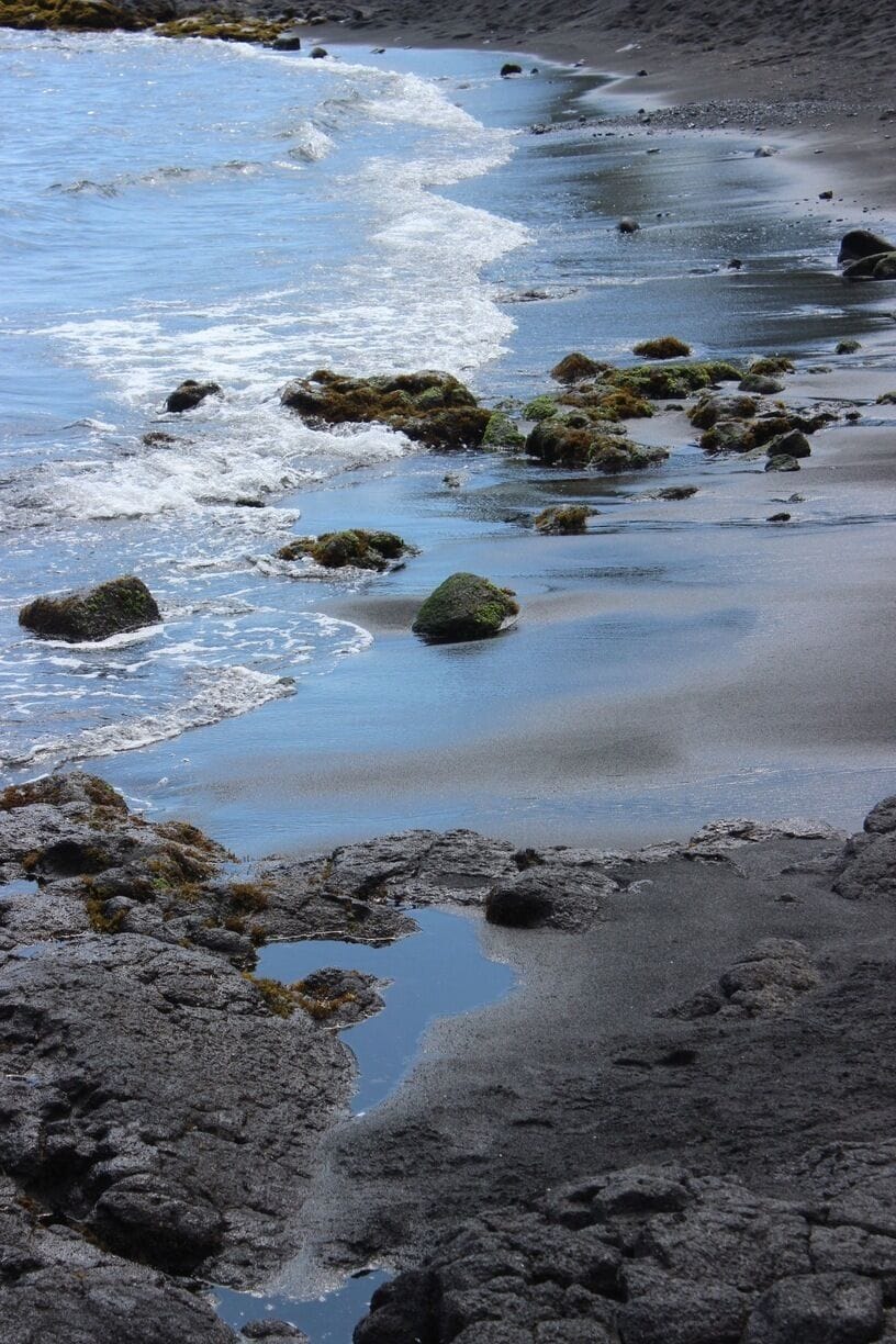 A rocky shoreline with waves gently lapping against the rocks and pebbles.
