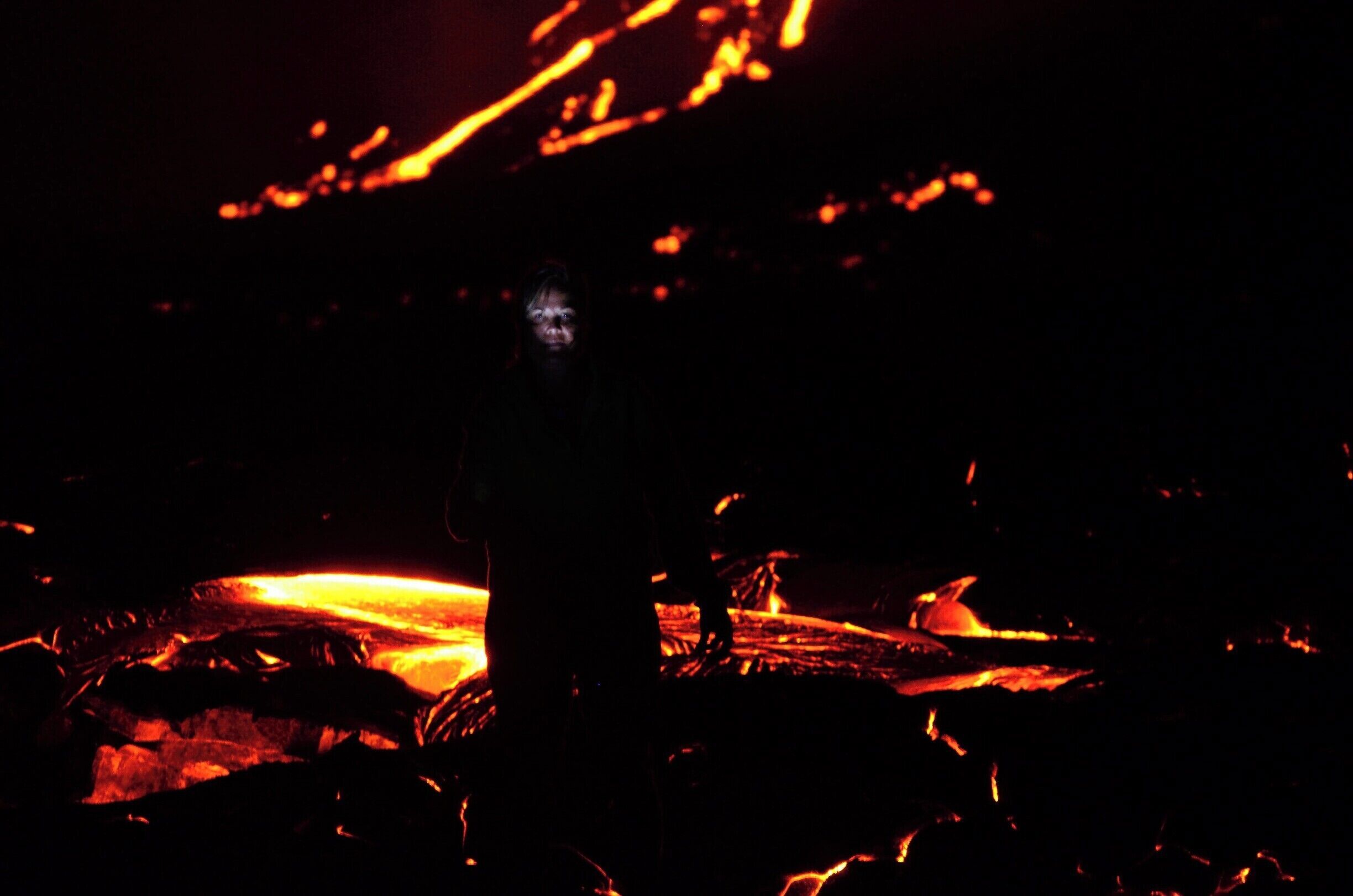 A silhouette of a person standing in front of a lava flow.