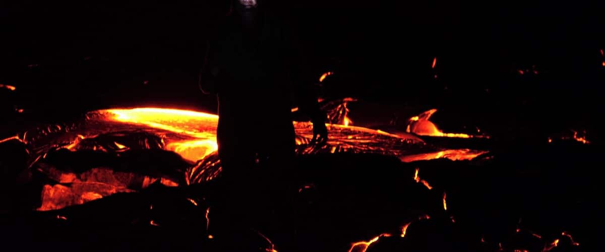 A silhouette of a person standing in front of a lava flow.