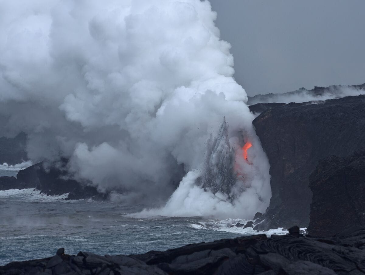 A volcanic eruption with lava flowing into the ocean, surrounded by rocky cliffs and mist.
