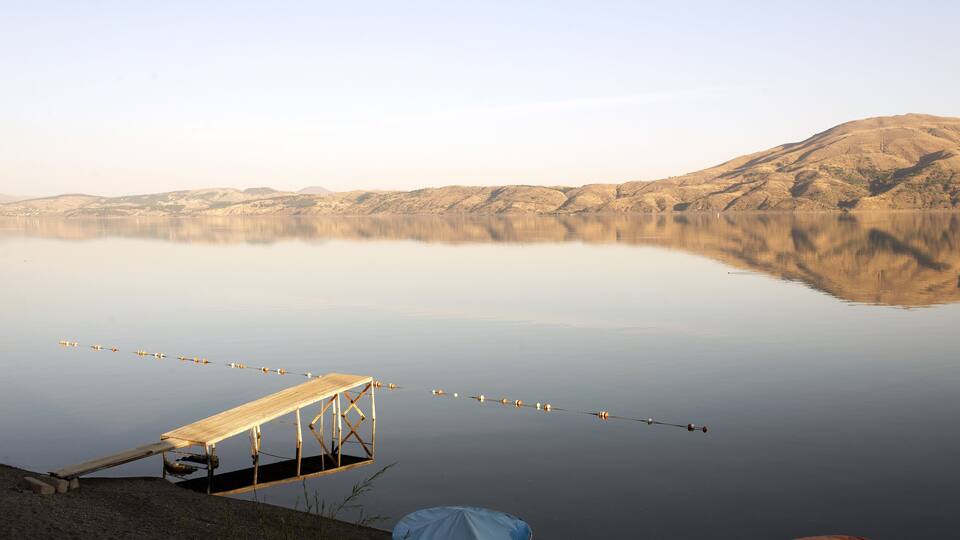 A calm lake with a wooden dock and fishing rods, surrounded by hills.