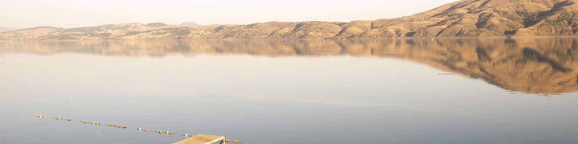 Un lago tranquilo con un muelle de madera y cañas de pescar, rodeado de colinas.
