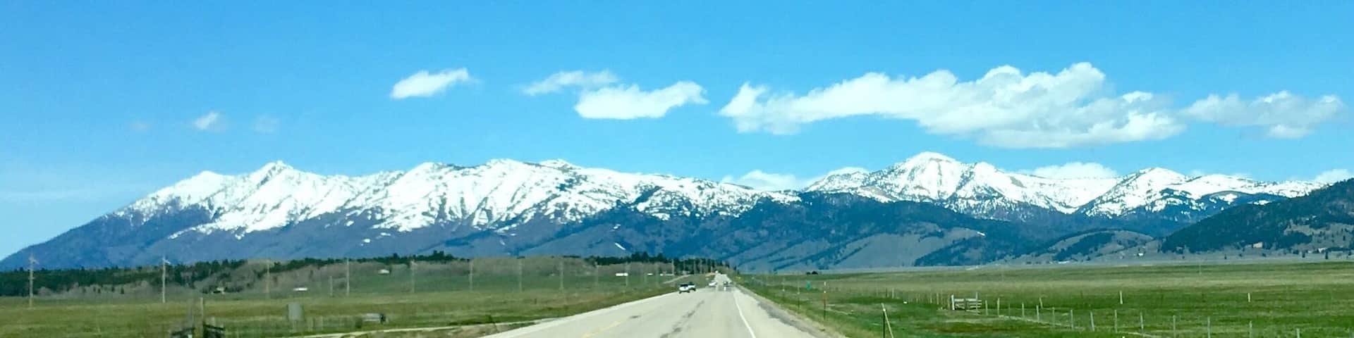 A road leading towards snow-capped mountains under a clear sky.