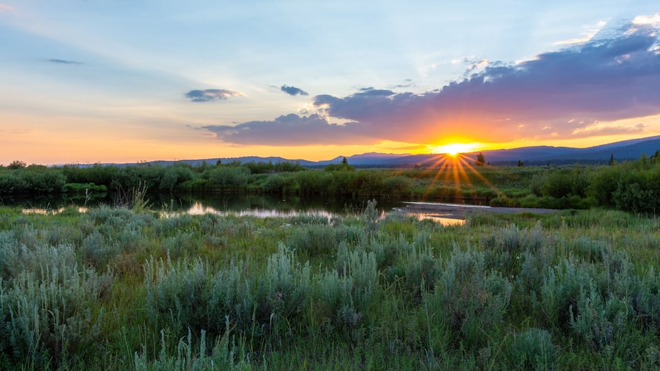 A sunset over a river with surrounding greenery and hills.