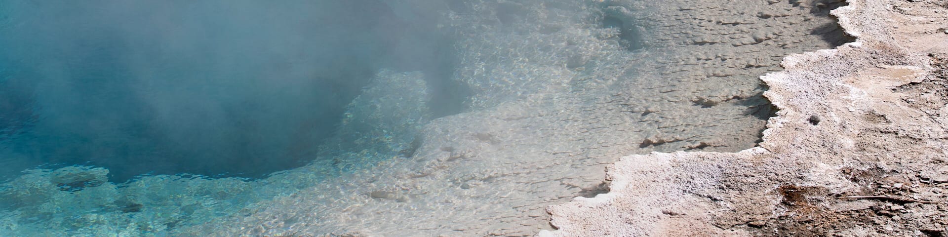 A clear aerial view of a geothermal area with mineral deposits and a body of water.