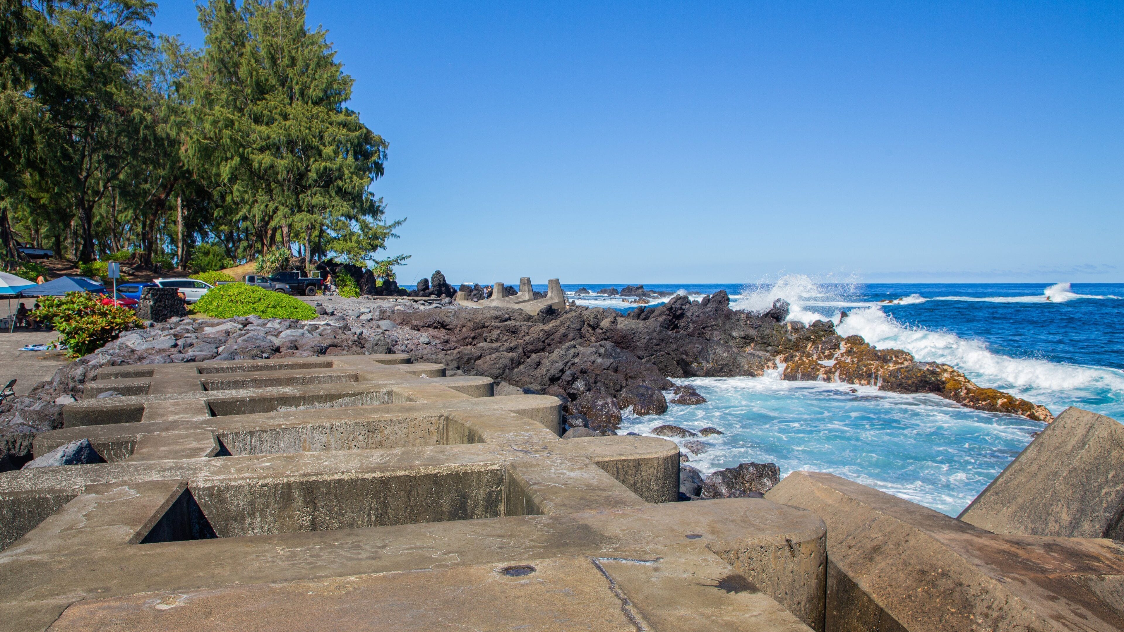 A coastal walkway with steps leading to the beach, surrounded by rocky terrain and ocean waves.