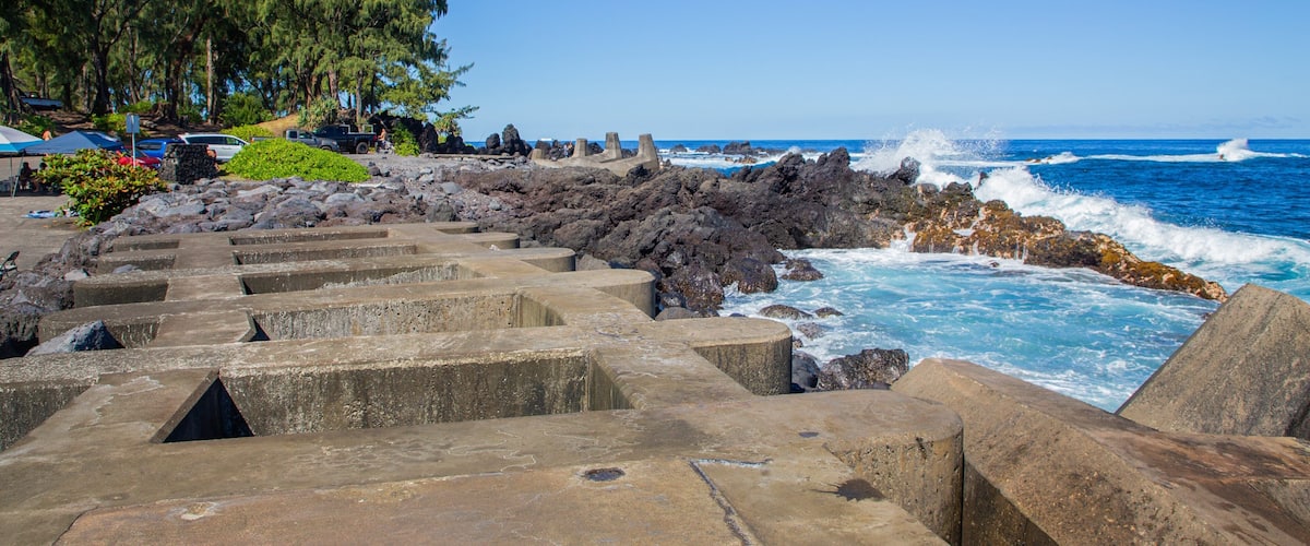 A coastal walkway with steps leading to the beach, surrounded by rocky terrain and ocean waves.
