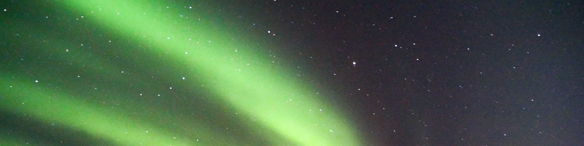 The Northern Lights over a snowy landscape with a cabin and people observing.