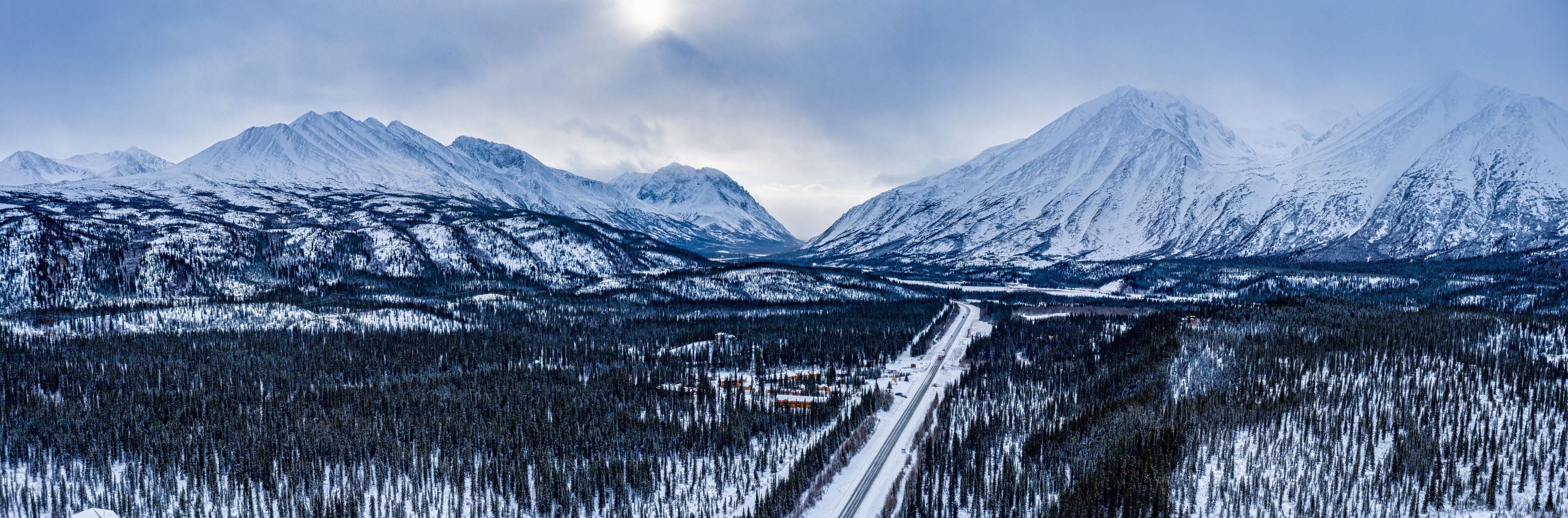 A snow-covered mountain range with a road leading through a forest.