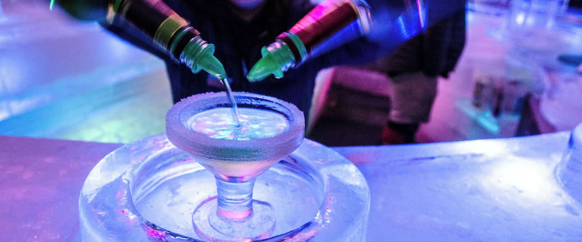 A person pouring a drink into a martini glass on an ice block.