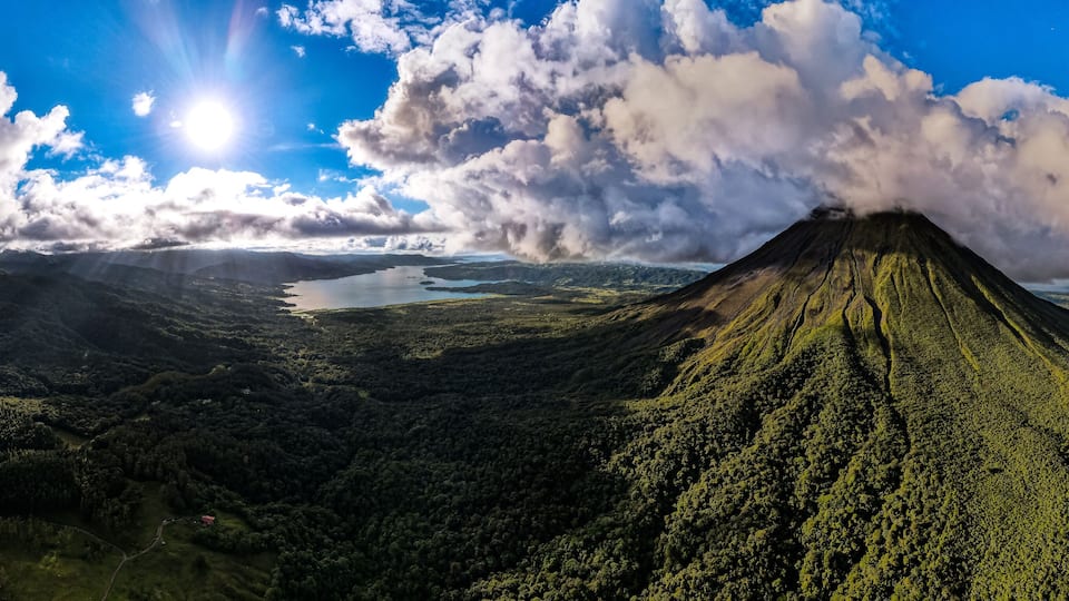 A volcano with a lake in the valley and a forested mountain range.