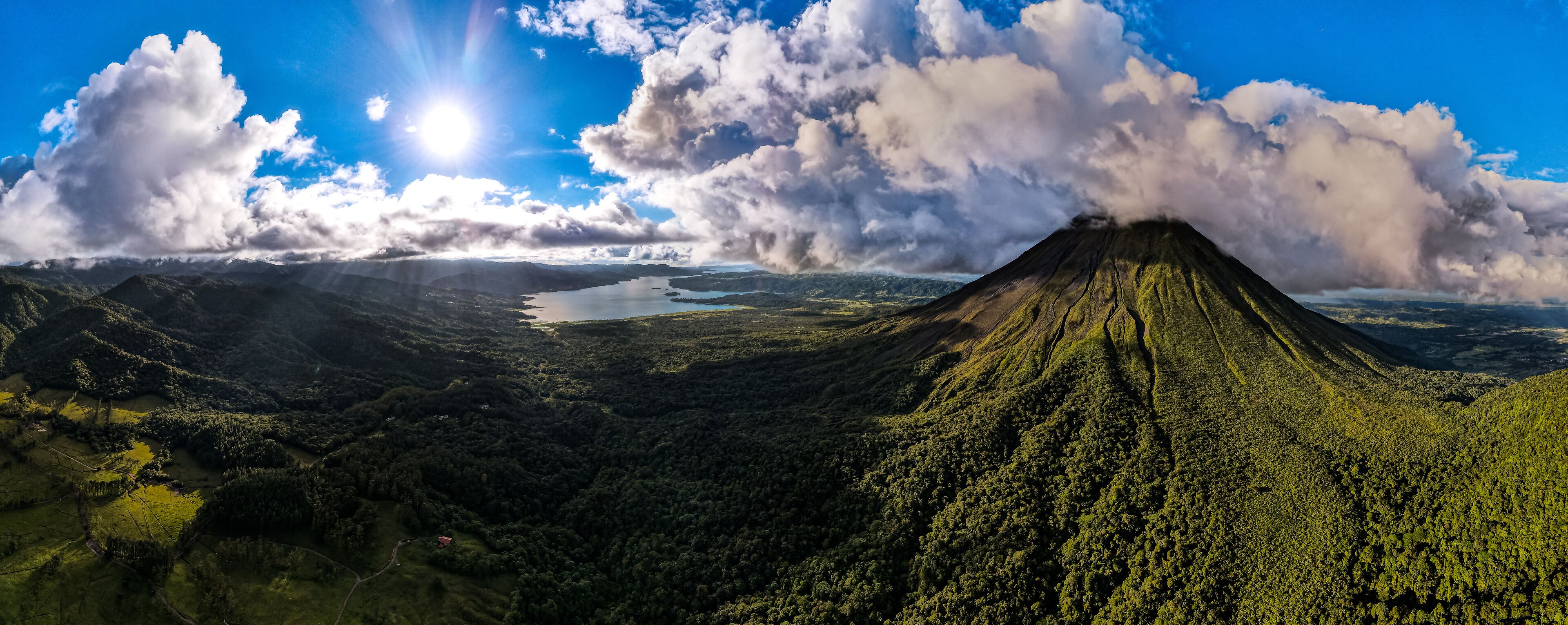 A volcano with a lake in the valley and a forested mountain range.