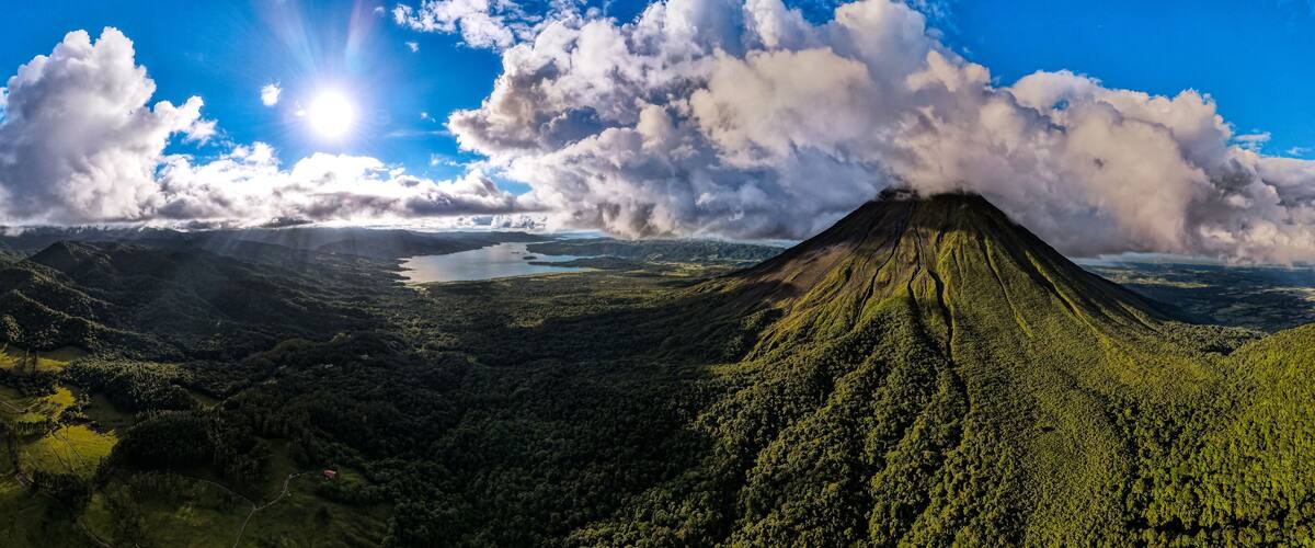 A volcano with a lake in the valley and a forested mountain range.