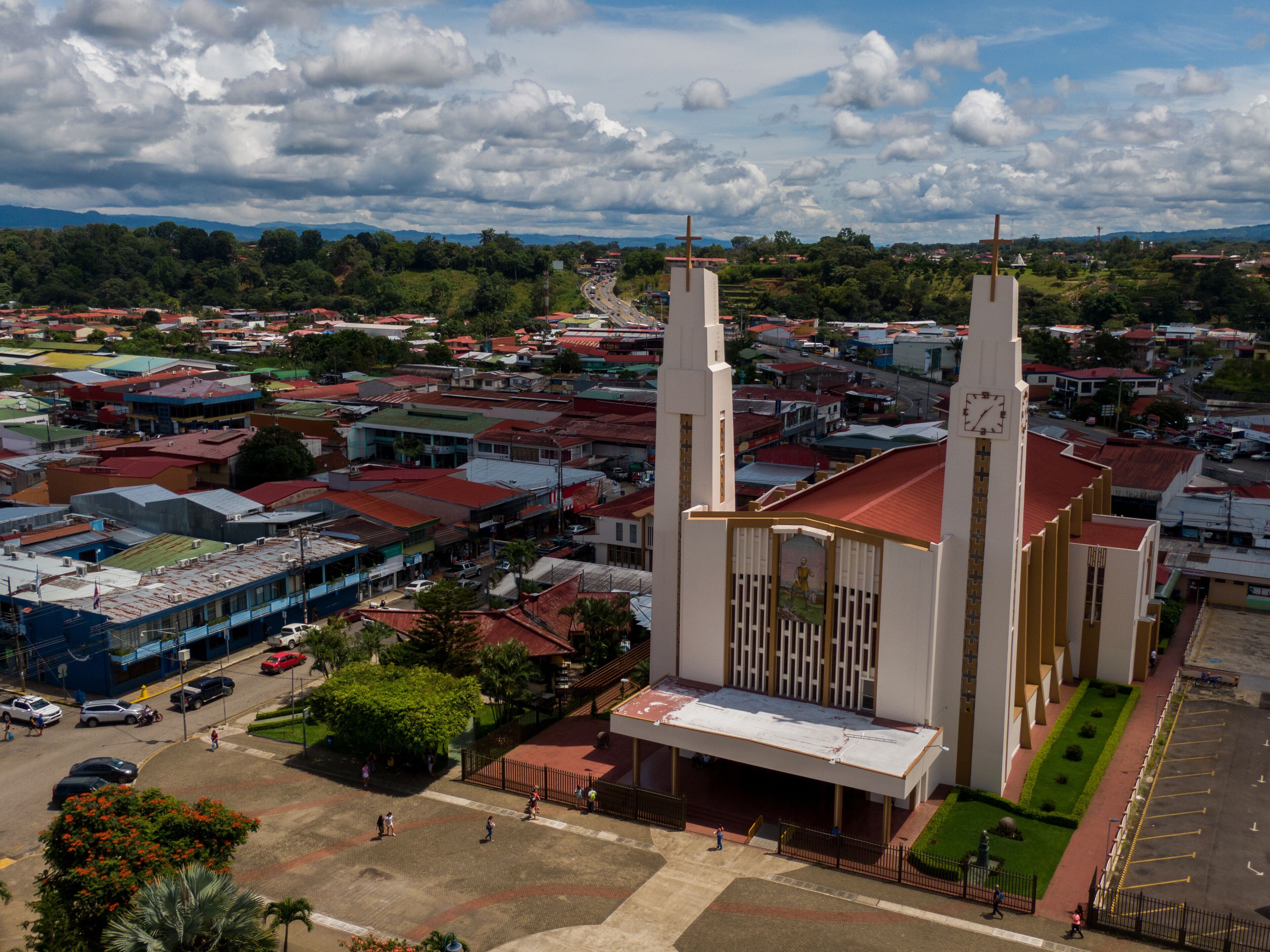 A large church with two towers and a clock, surrounded by a cityscape with red-roofed buildings.