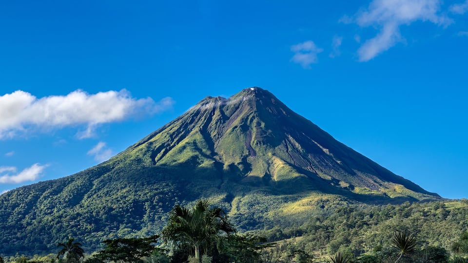 A mountain with a peak, surrounded by lush green vegetation and a clear blue sky.
