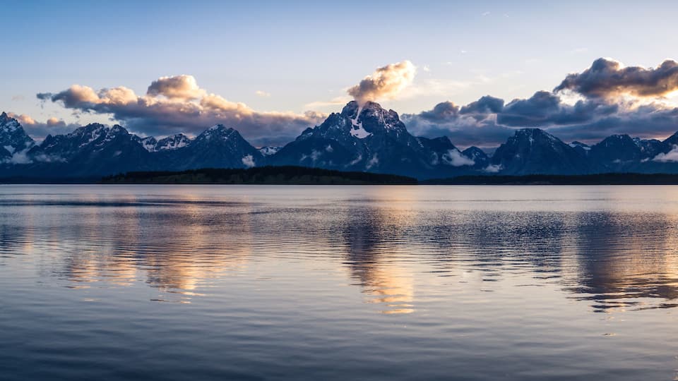 A mountain range with snow-capped peaks reflected in calm water.