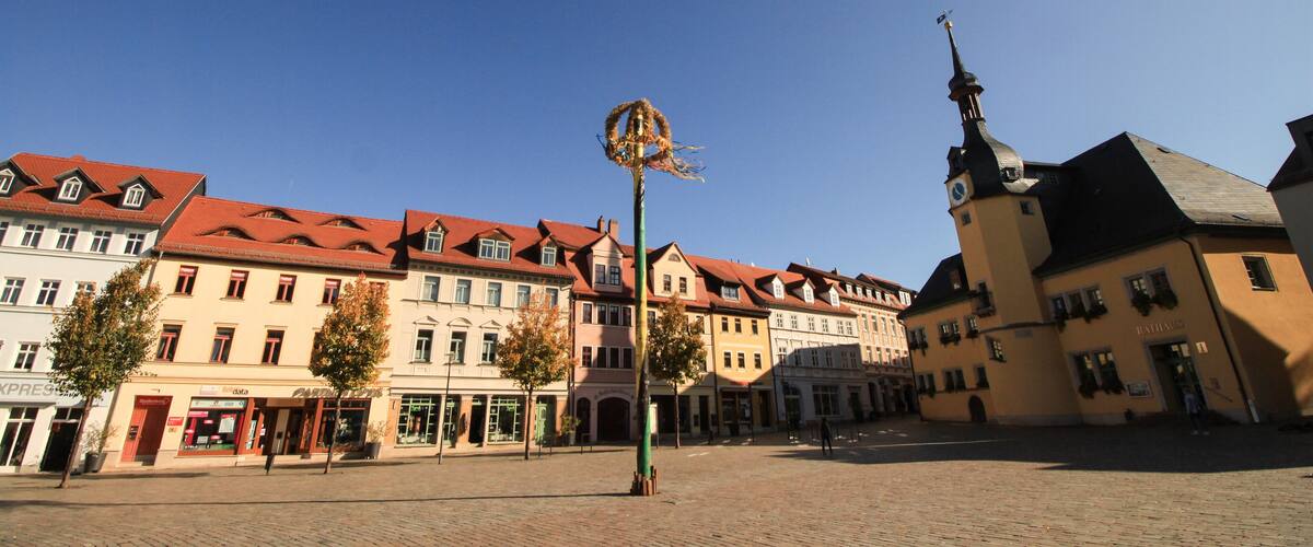 A cobblestone square with historic buildings, a clock tower, and a decorative post.